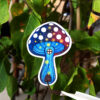Sticker holographique d'un champignon bleu et rouge avec des pois blancs, il est accompagné de petites étoiles qui renforcent son côté magique.Sticker holographique d'un champignon bleu et rouge avec des pois blancs, il est accompagné de petites étoiles qui renforcent son côté magique.